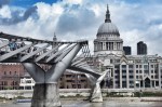 A view of the Millennium Bridge in front of St. Paul's Cathedral, featuring a cloudy sky and city skyline in the background.