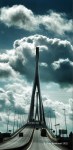 A modern suspension bridge with a tall, slender tower, set against a backdrop of dramatic clouds.