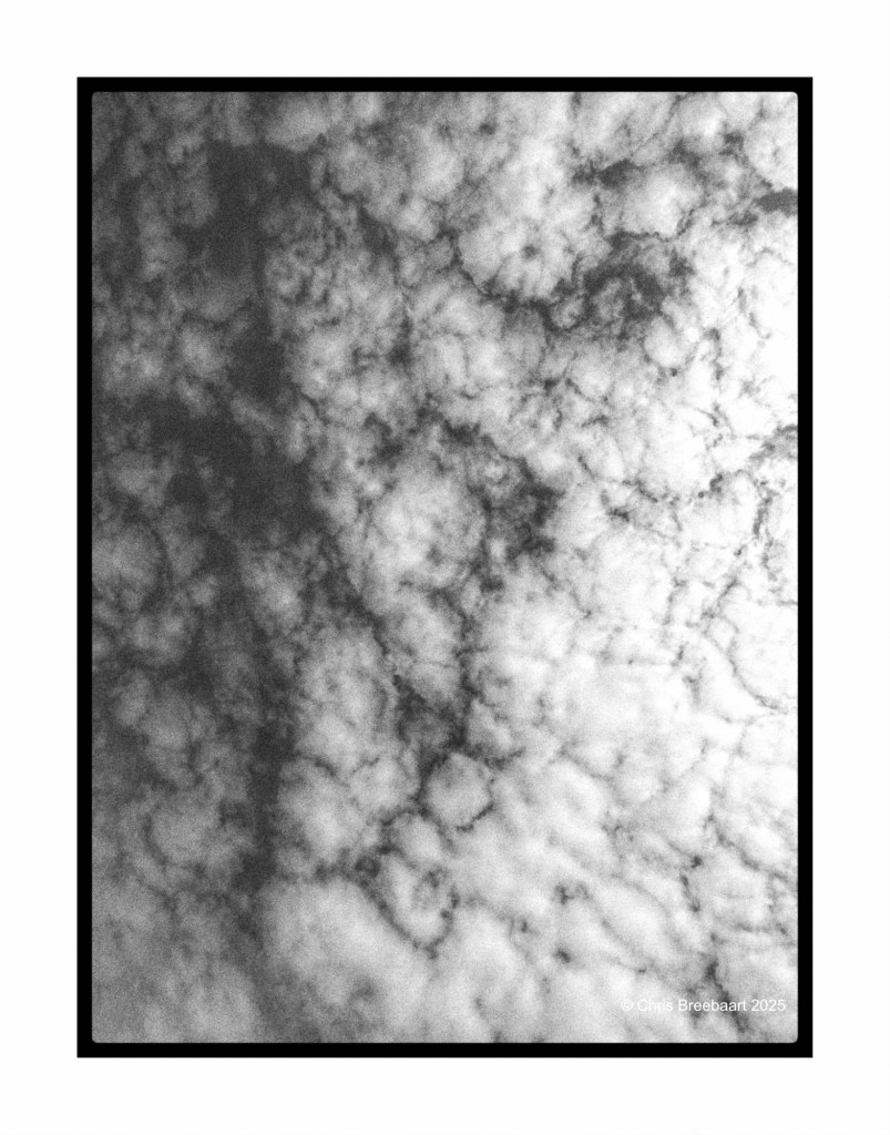 A black and white monochrome image of a cloudy sky, featuring various shades of gray and white, creating an abstract and mysterious atmosphere.