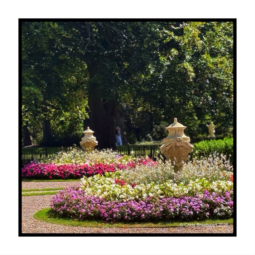 Colorful flower beds in the garden of Keukenhof castle, featuring decorative stone urns and lush greenery.