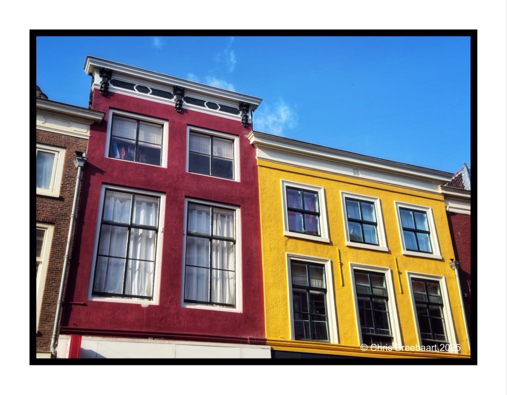 Fronts of houses in Breestraat, Leiden, featuring red and yellow facades under a blue sky.