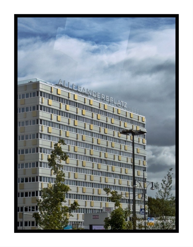 A modern building featuring the sign 'Allesandersplatz' against a cloudy sky in Berlin.