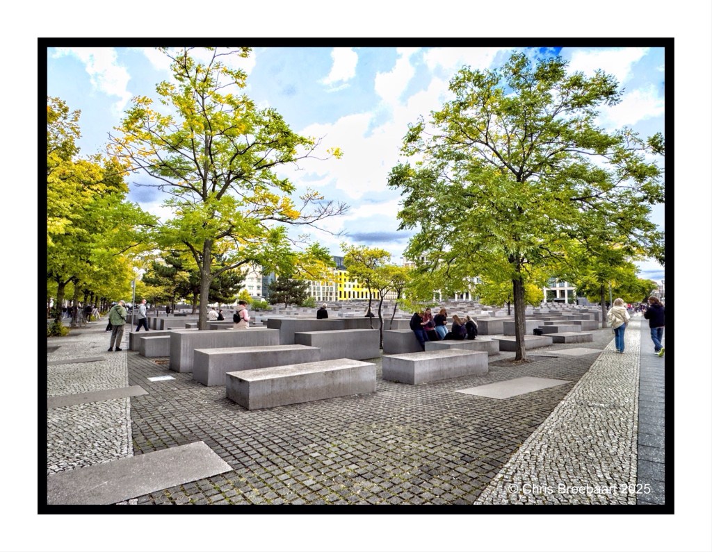 View of the Memorial to the murdered Jews in Europe, featuring a series of concrete slabs and trees, with visitors walking and sitting among the memorial structures.