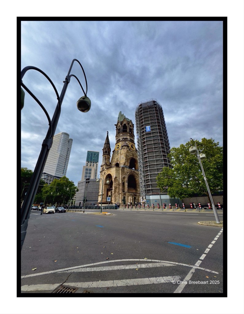 View of the Kaiser Wilhelm Gedächtnis Kirche, a memorial church in Berlin, surrounded by modern buildings, with cloudy skies overhead.