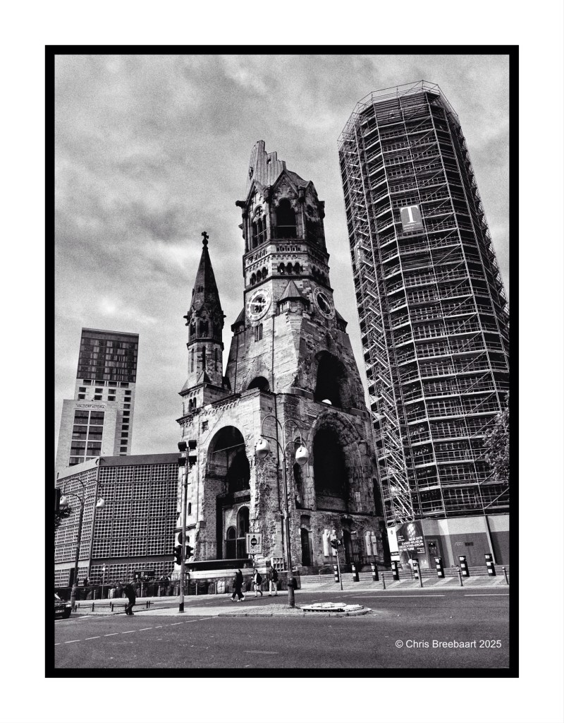 Black and white photograph of the Kaiser Wilhelm Memorial Church in Berlin, showcasing its historic architecture alongside modern buildings.