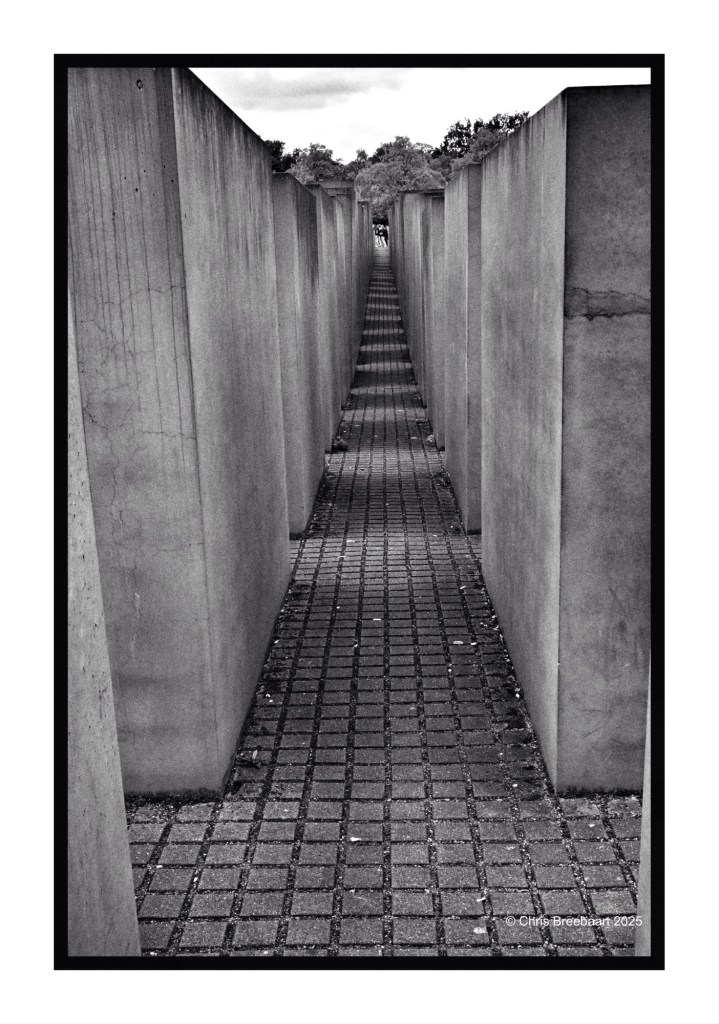 A narrow pathway lined with tall concrete slabs at the Memorial to the Murdered Jews of Europe in Berlin, captured in black and white.