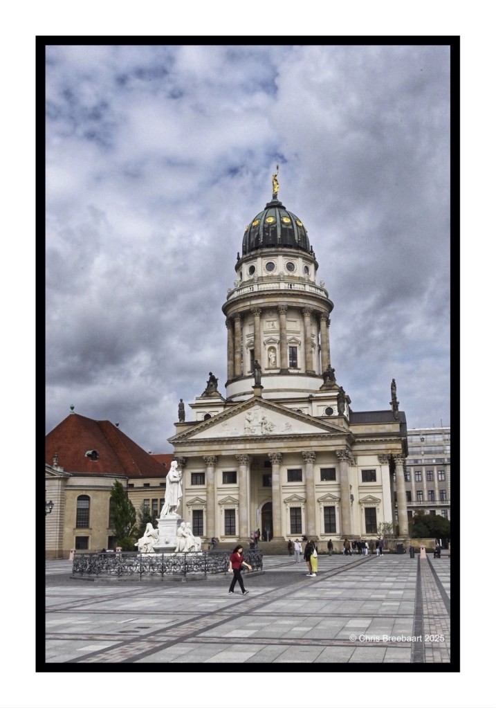 A view of the Deutscher Dom (German Cathedral) at Gendarmenmarkt in Berlin, featuring its ornate dome and statues, with visitors strolling in the square.