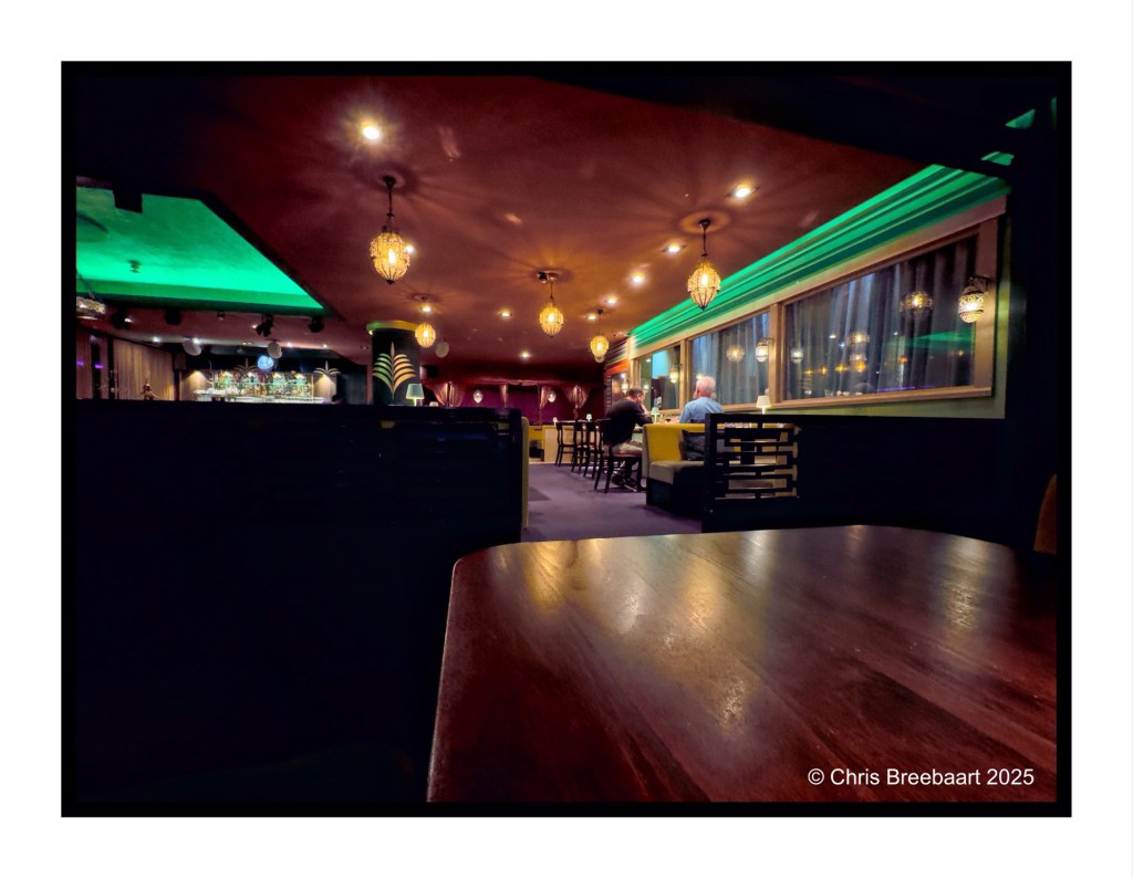 Interior view of a dimly lit restaurant in Berlin, featuring green and orange lighting, decorative hanging lamps, and wooden furniture.