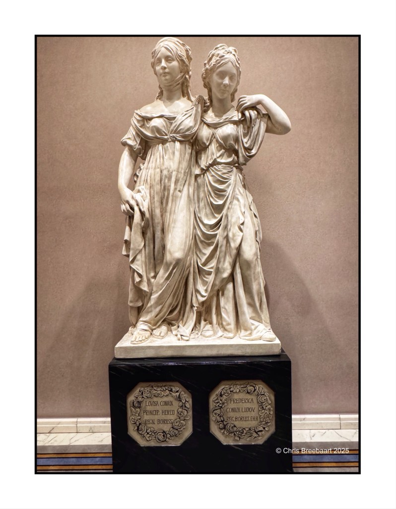 A marble statue of two women in elegant attire, displayed on a pedestal with inscriptions, located in a hotel lobby.
