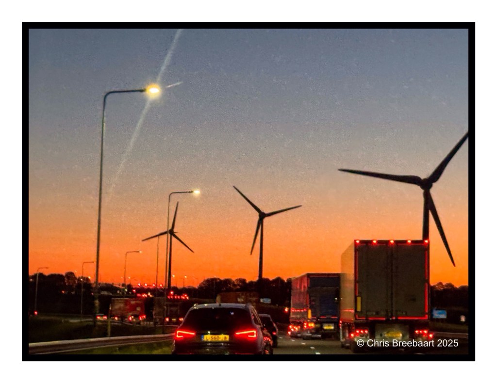 A scenic view of the A44 and A4 highways leading to Schiphol Amsterdam at sunrise, featuring silhouetted wind turbines and vehicles on the road.