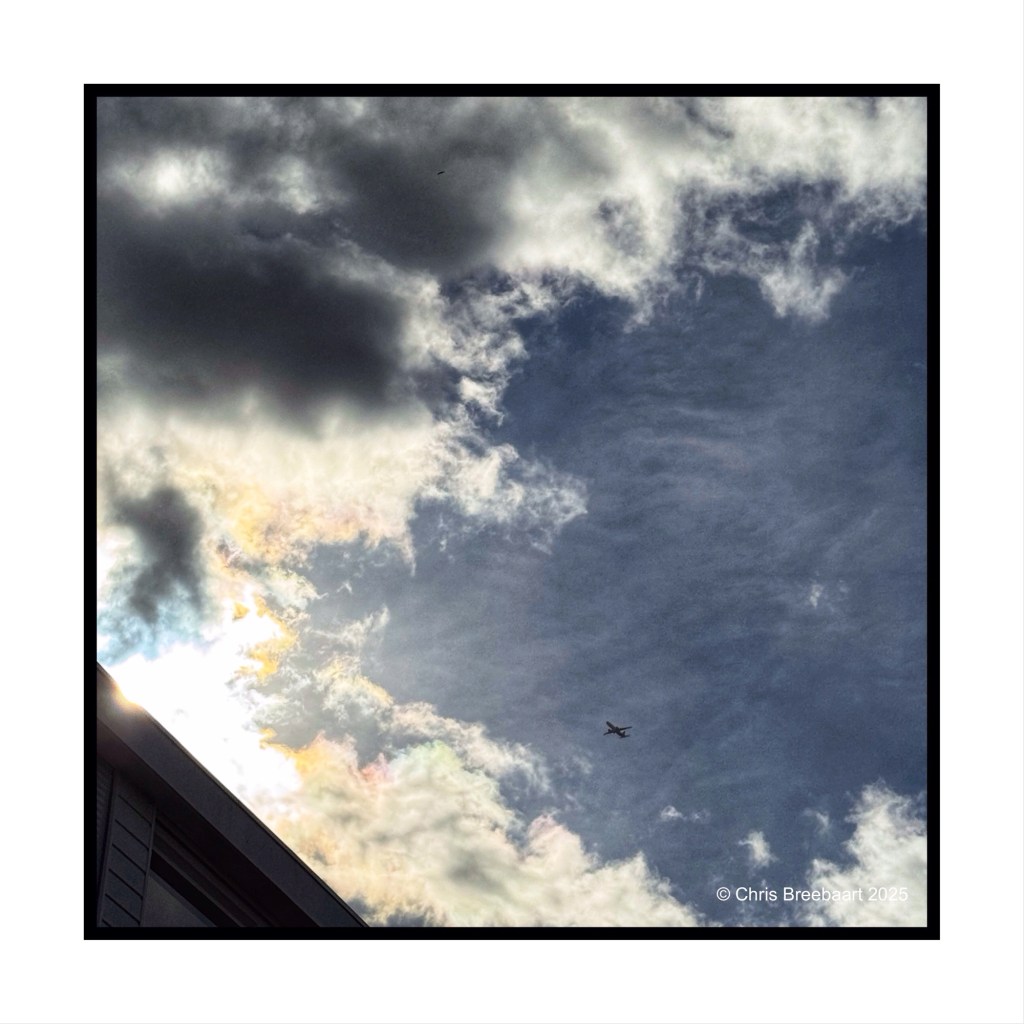 A dynamic sky filled with clouds in various forms and colors, with sunlight peeking through and a small airplane flying in the distance.