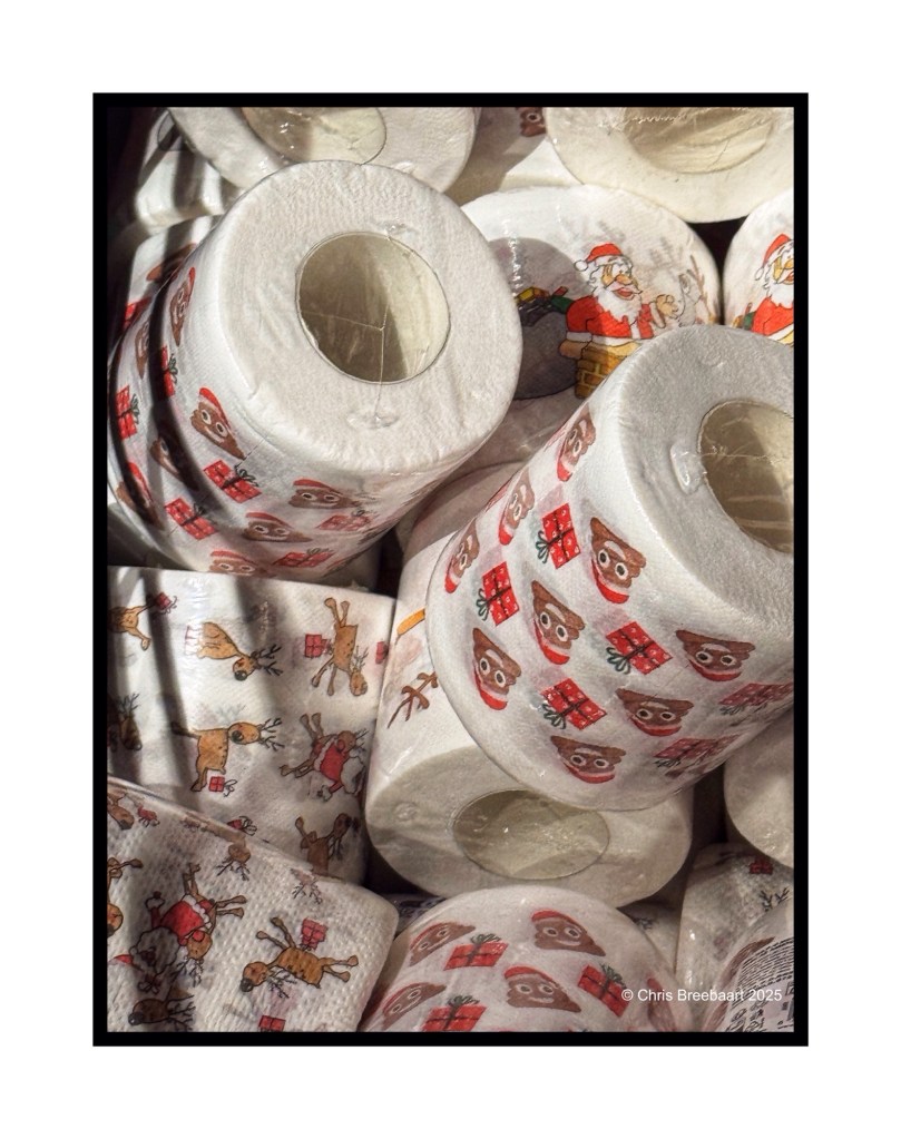 A close-up view of rolls of toilet paper decorated with festive Christmas-themed designs, including Santa Claus and reindeer, stacked together.