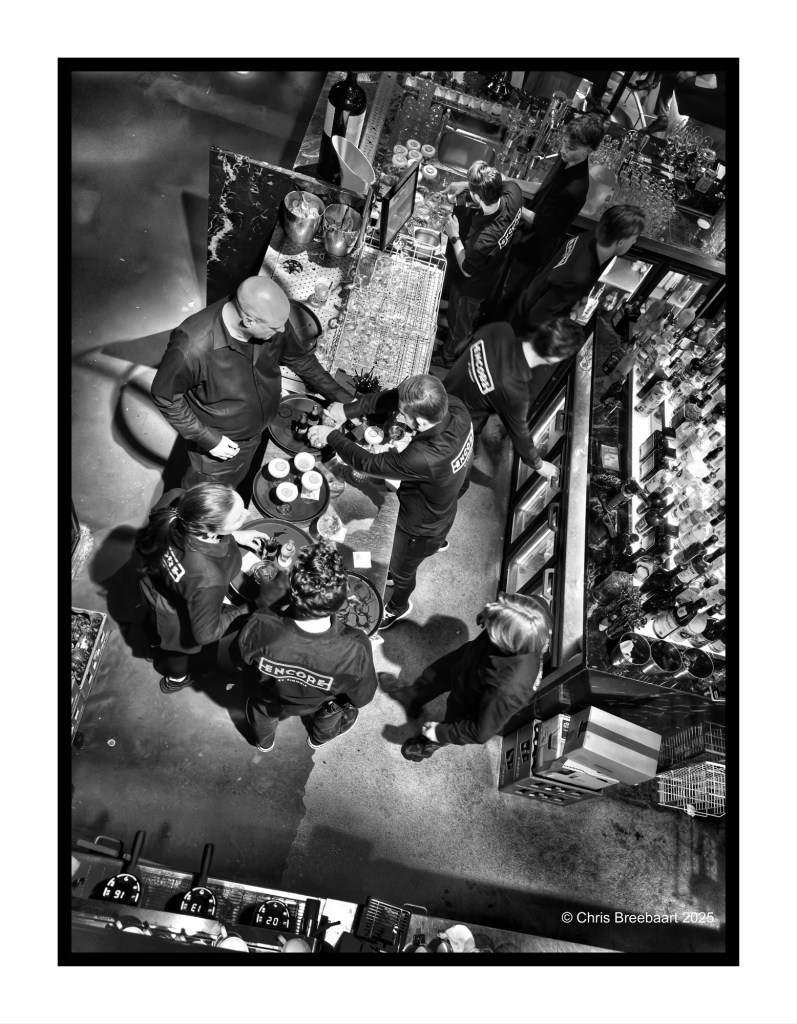 Aerial view of a bustling bar scene at an end-of-year event, with staff dressed in black uniforms interacting and serving drinks against a backdrop of bottles and bar equipment.