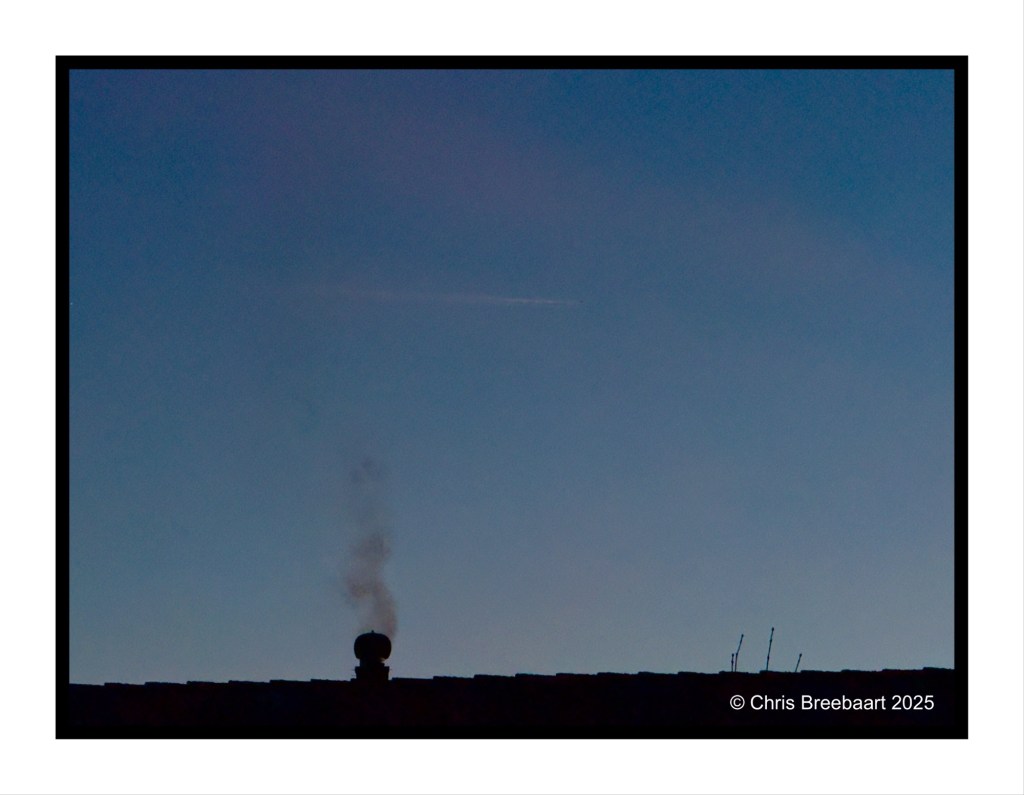 Silhouette of a rooftop with smoke rising from a chimney against a blue sky.