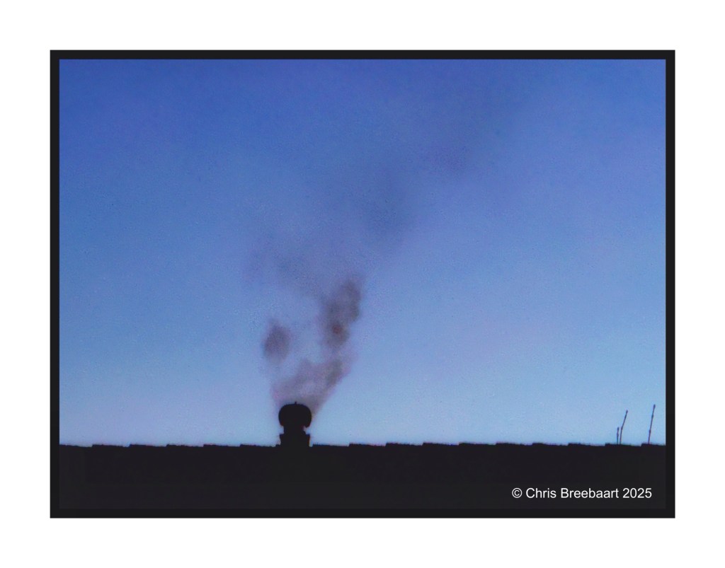 Silhouette of a chimney with smoke against a twilight sky.