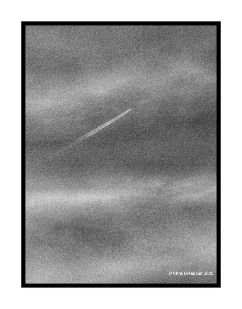 A black and white image of a cloud-filled sky with a faint contrail running diagonally across the frame.