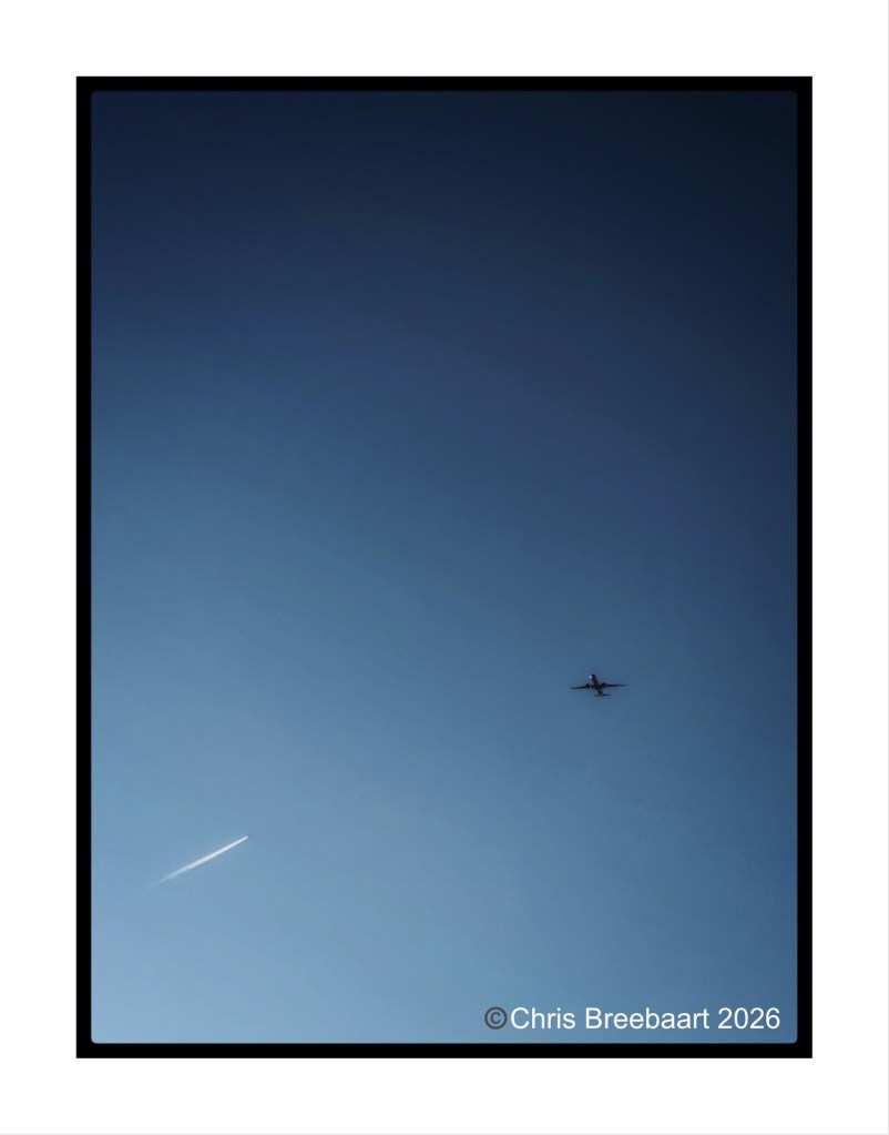 An airplane flying in a clear blue sky with a contrail trailing behind it.