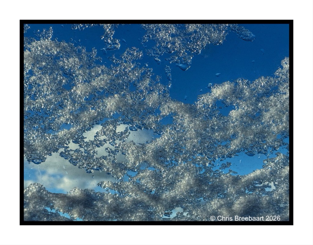 Close-up view of ice crystals against a blue sky, showcasing intricate snowflakes and sparkling frost.