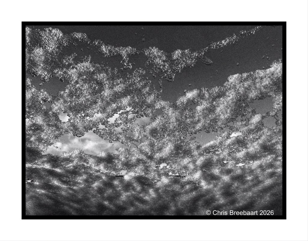 Black and white image of a textured sky filled with clouds, showing varying shades and patterns.