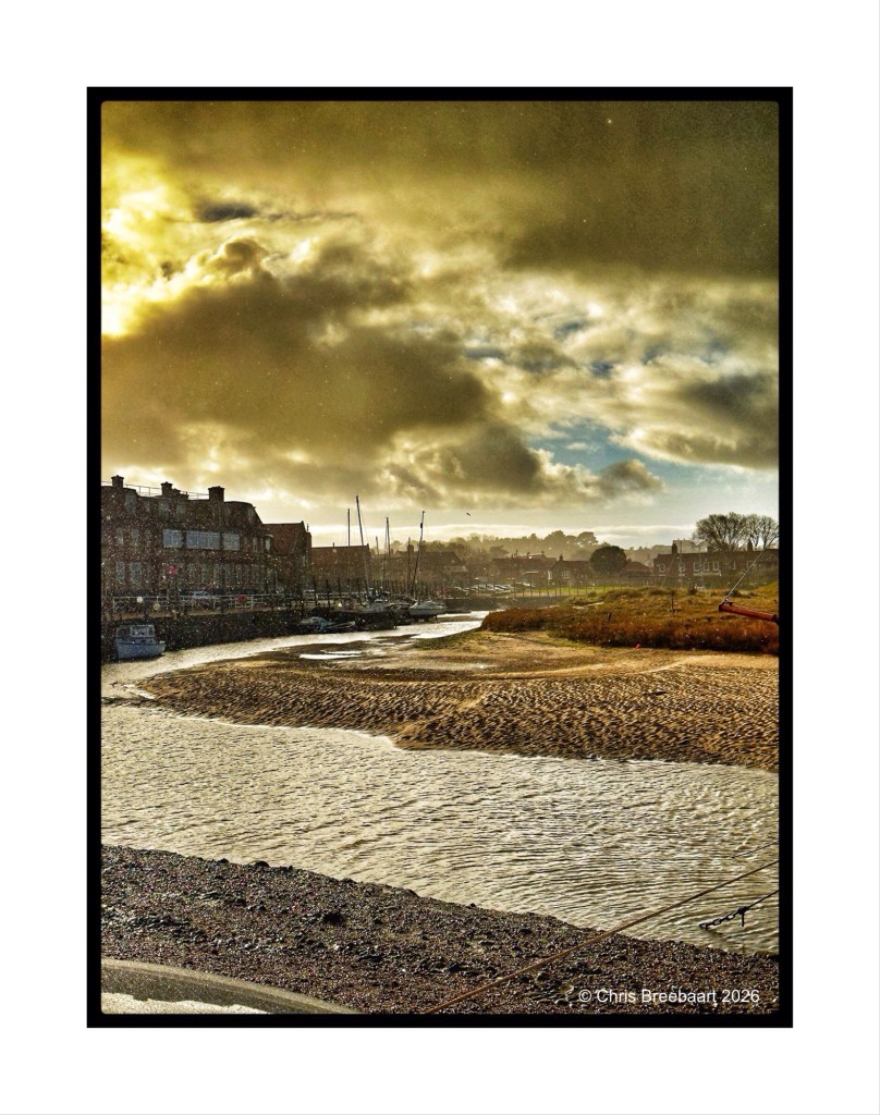A scenic view of a riverbank scene with buildings on one side, a sandy area in the foreground, and dramatic clouds in the sky, capturing the beauty of nature and architecture.