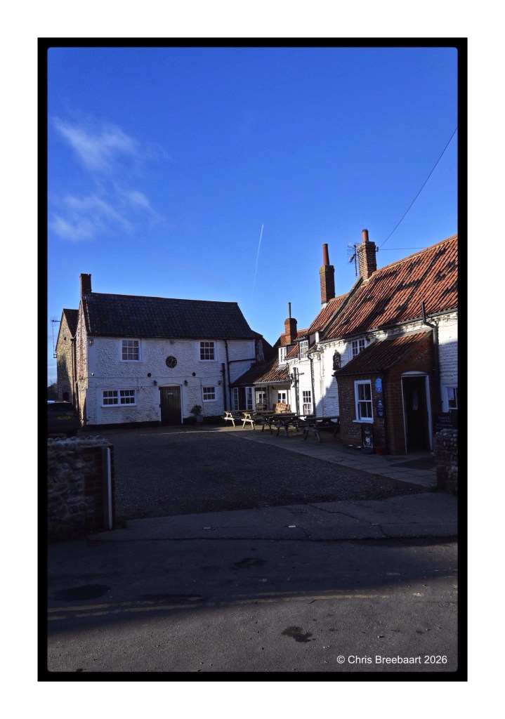 A picturesque village square featuring traditional architecture with red-tiled roofs, surrounded by several buildings and a clear blue sky.