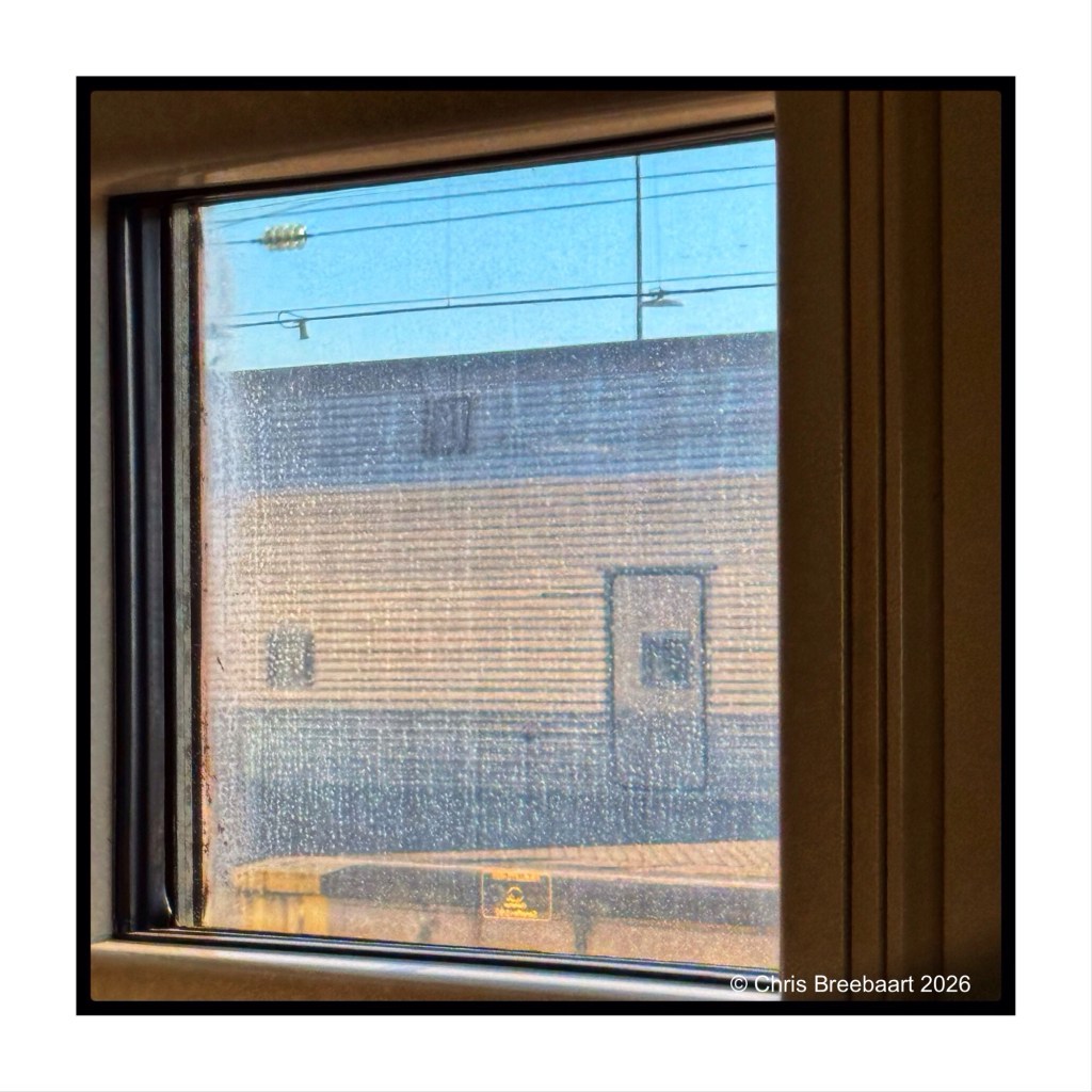 View through a window showing a blurred exterior with a blue sky and a building in the background, featuring lines and texture on the glass.