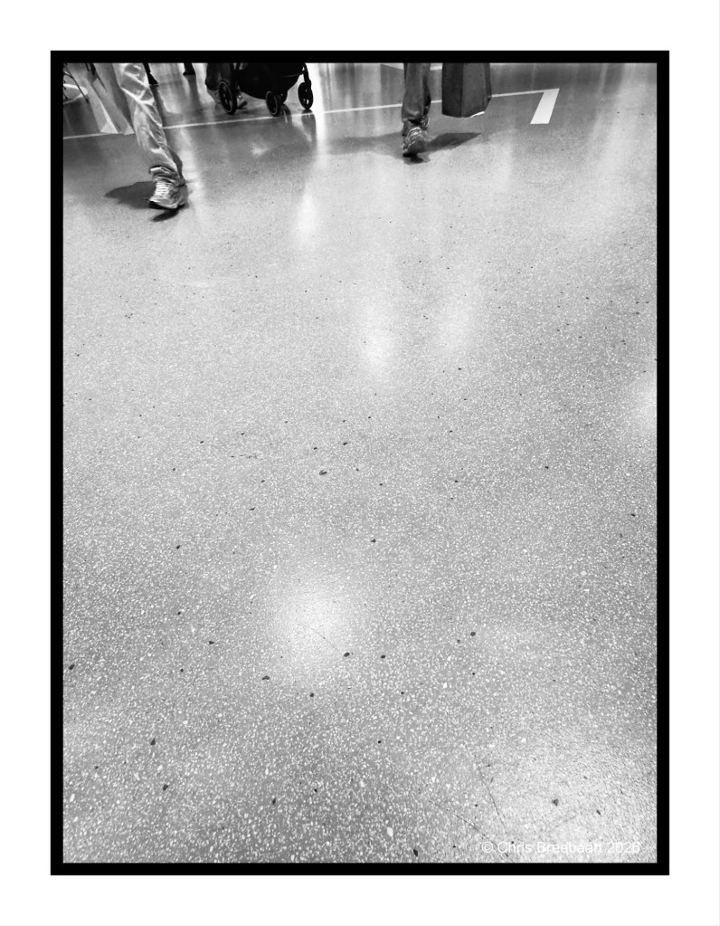 Close-up view of the floor in a busy indoor space with people walking, captured in black and white.
