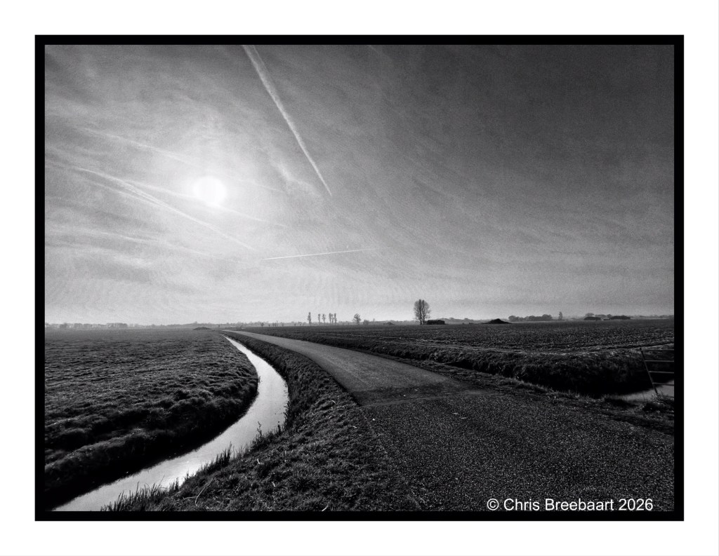 A black and white landscape featuring a winding road beside a small canal, under a cloudy sky with the sun visible.