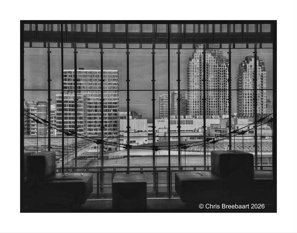 Black and white view of modern city skyscrapers through a large glass window, with contemporary seating in the foreground.