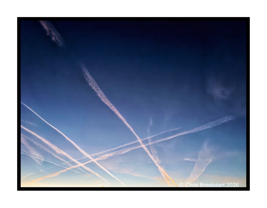 A clear sky with multiple contrails forming intersecting lines against a gradient blue backdrop.