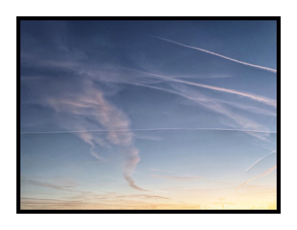 A colorful sky at dusk featuring wispy clouds and airplane contrails, creating a serene atmosphere.