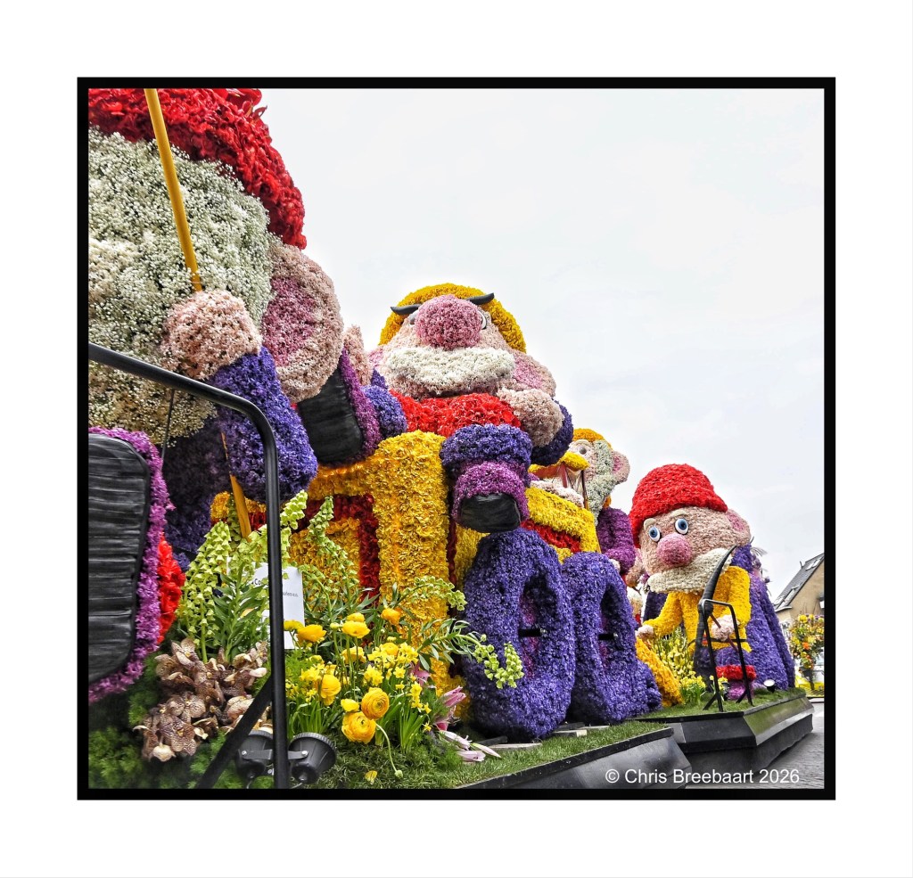 Colorful floral floats featuring whimsical characters at a parade, decorated with various flowers.