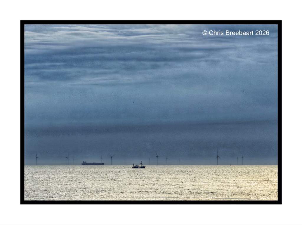 A coastal view featuring a ship on calm waters, with wind turbines visible in the background under a cloudy sky.