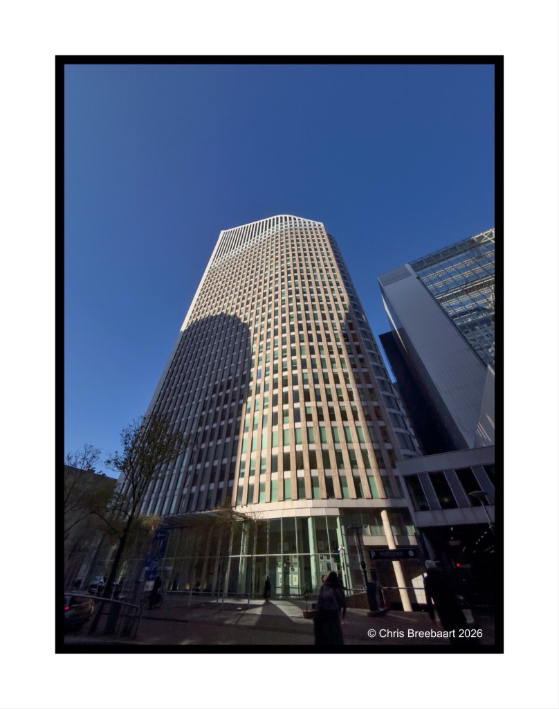 Tall modern office building with glass facade and a clear blue sky in the background.
