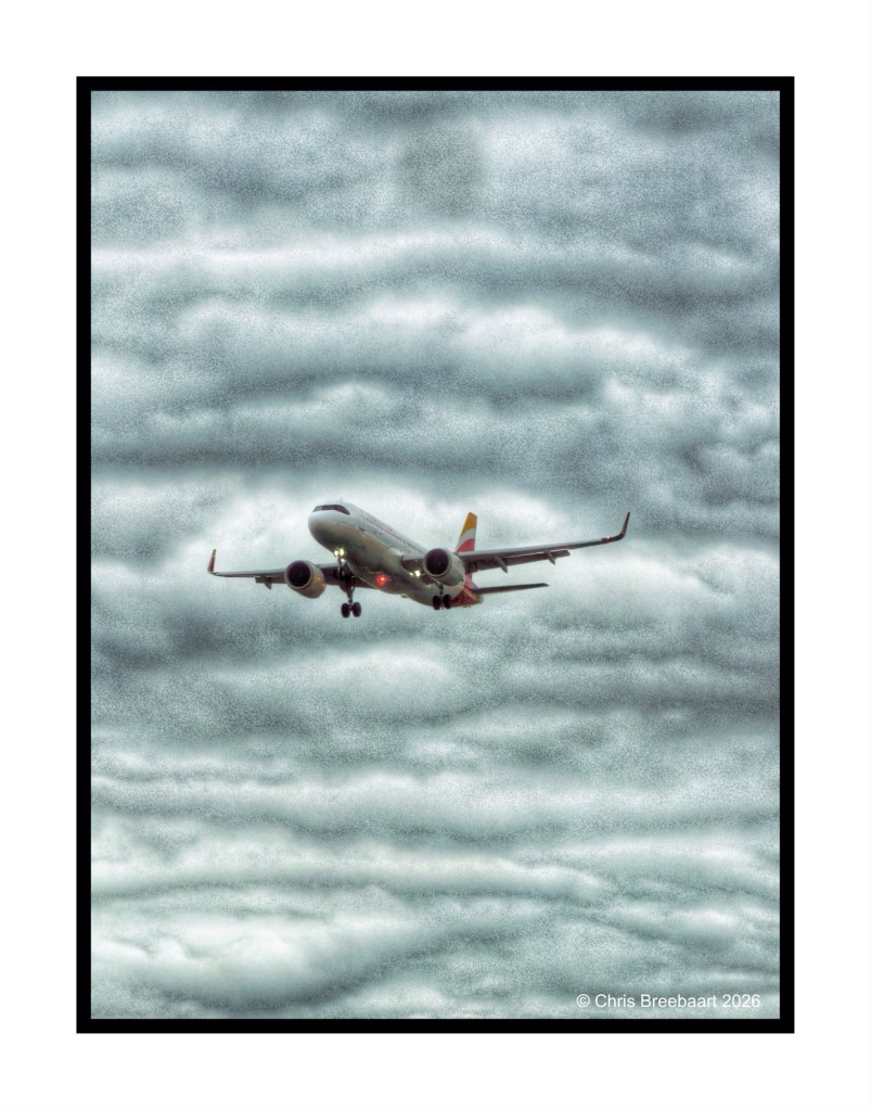 An airplane flying through a cloudy sky, with gray clouds in the background.
