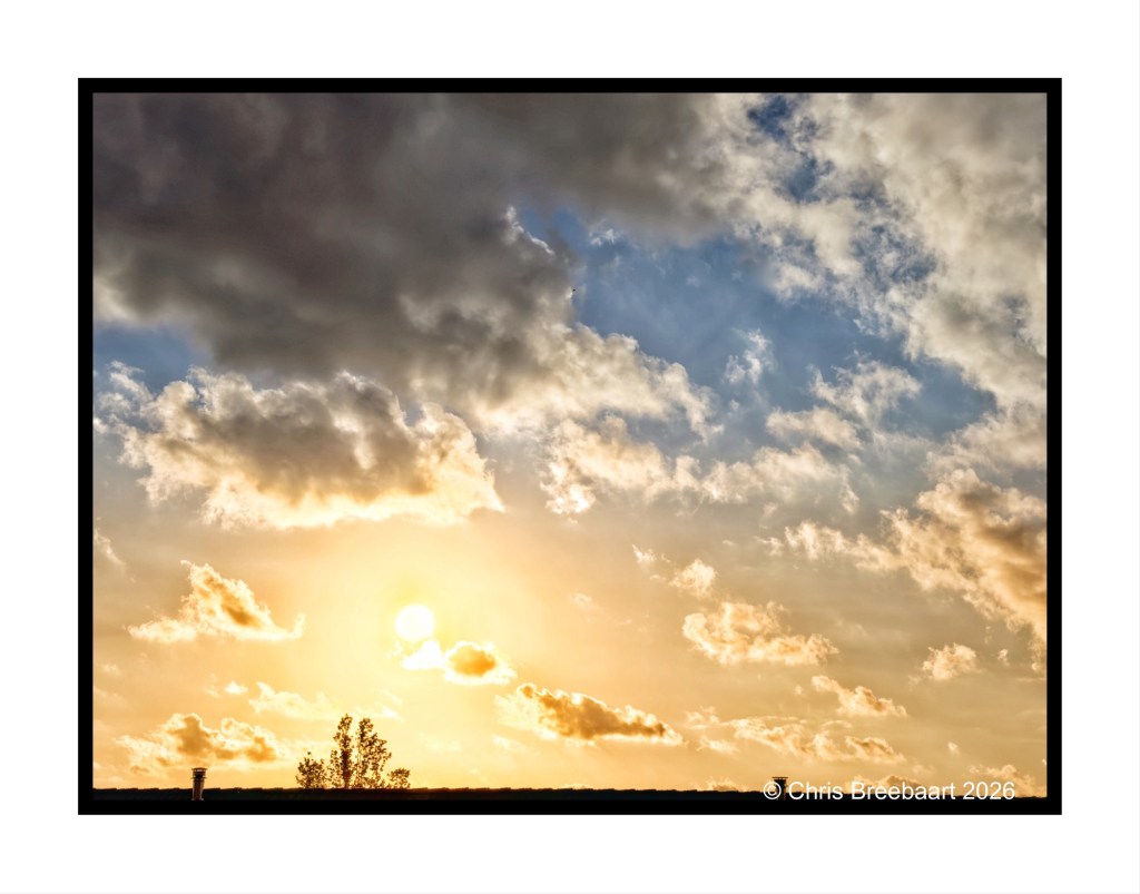 A beautiful sunset with bright orange and yellow hues illuminating the sky, surrounded by soft clouds and a hint of blue in the background.