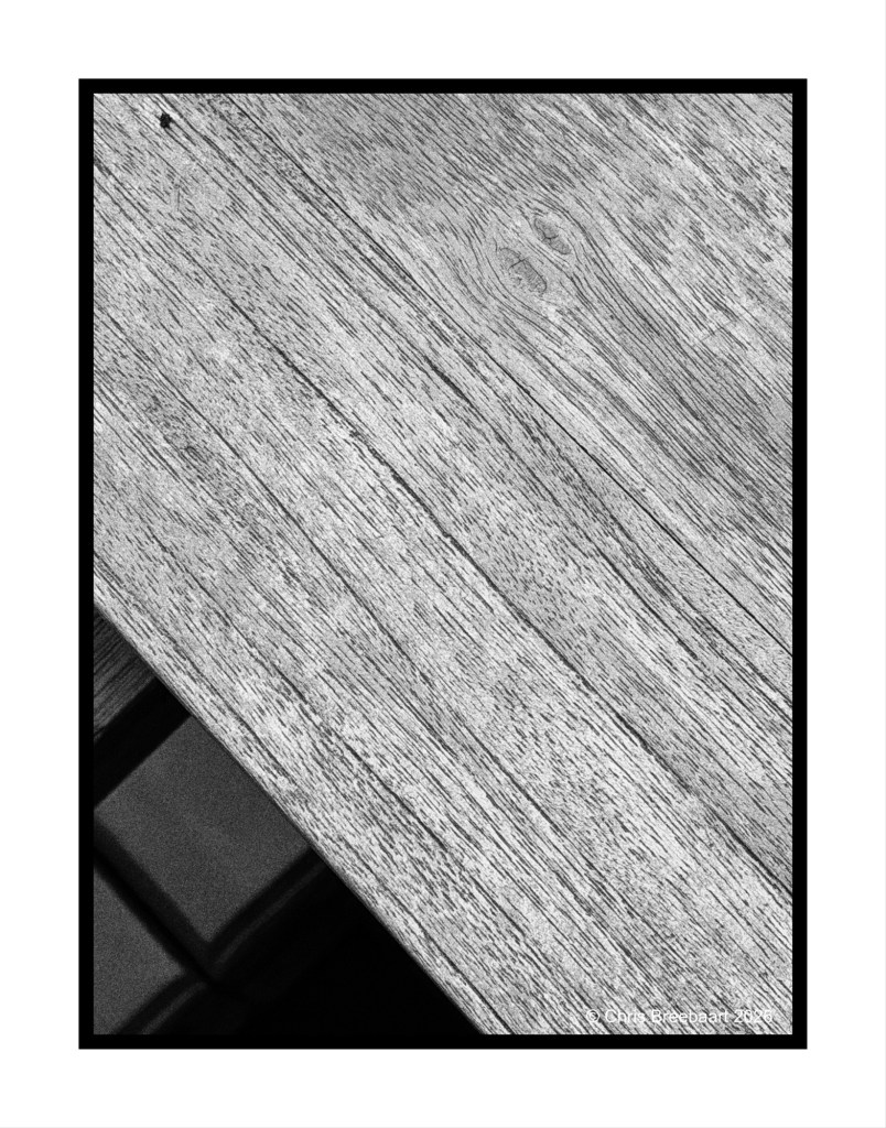 Close-up of a textured wooden surface in black and white, showing grain patterns and shadows.