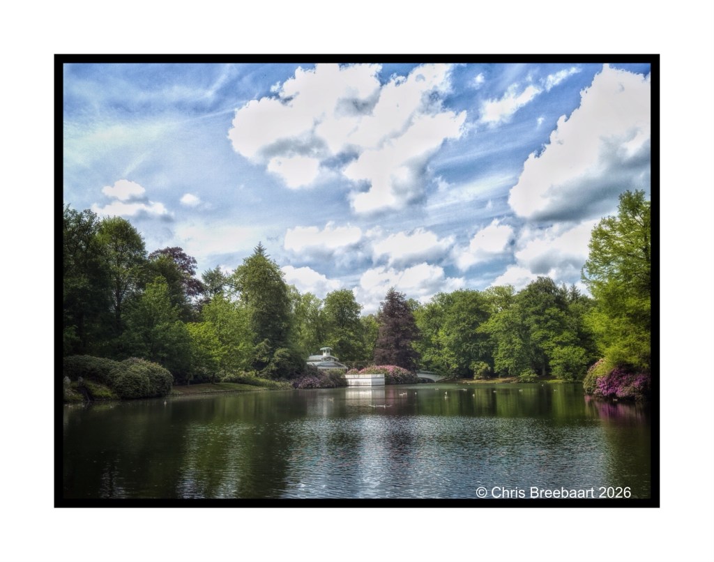 A serene pond surrounded by lush greenery and blooming trees under a bright blue sky with fluffy white clouds.