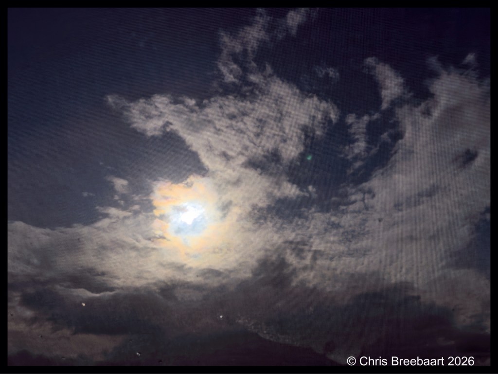 A cloudy sky with the sun peeking through, creating a halo effect around it.