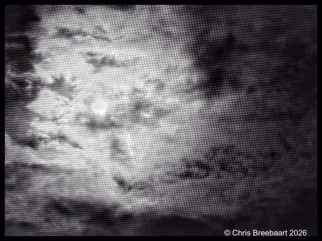 Black and white image of a cloudy sky with a visible sun behind the clouds, featuring a textured, dot-pattern overlay.