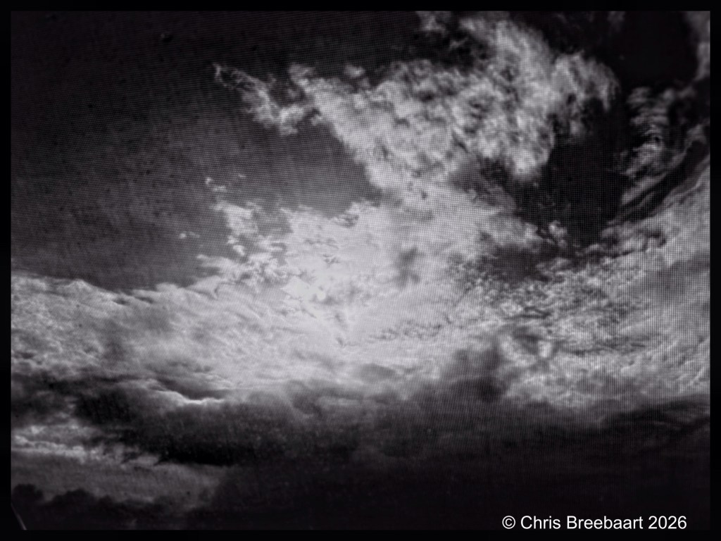 Dramatic black and white image of a cloudy sky with varying cloud formations and light peeking through.