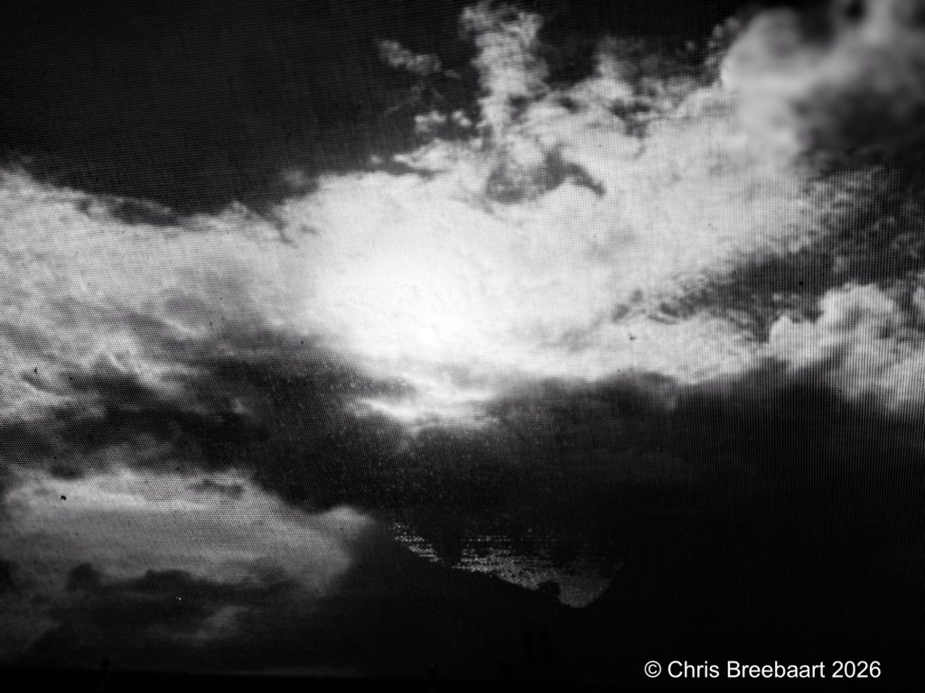 A black and white image of a cloudy sky with light peeking through, creating a dramatic atmosphere.