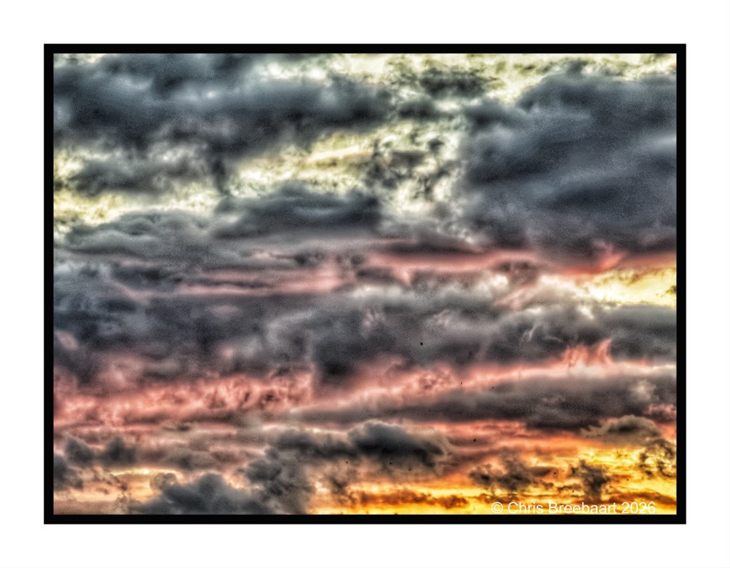 Dramatic sky at sunset featuring layered clouds in shades of gray, pink, and orange.