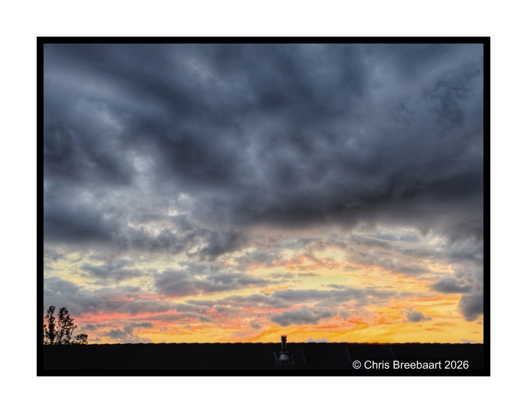Dramatic sunset scene with dark clouds and colorful hues of orange and pink on the horizon.