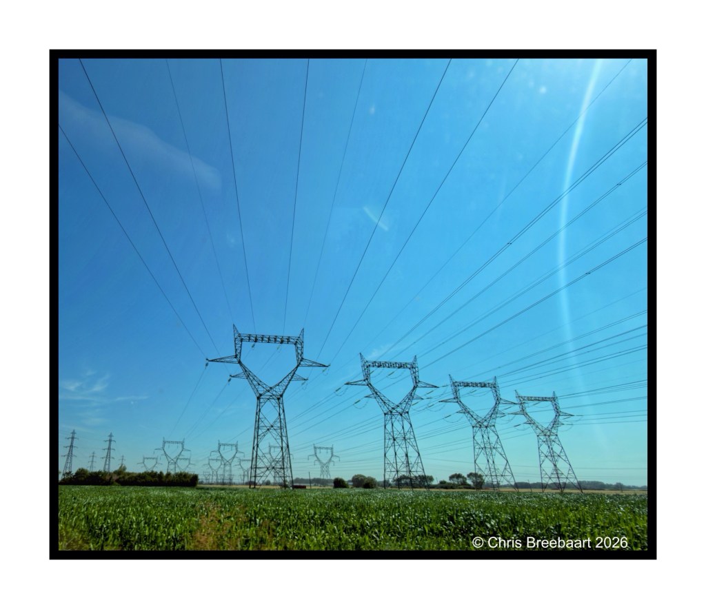 Electricity transmission towers against a clear blue sky, with power lines stretching over a green field.