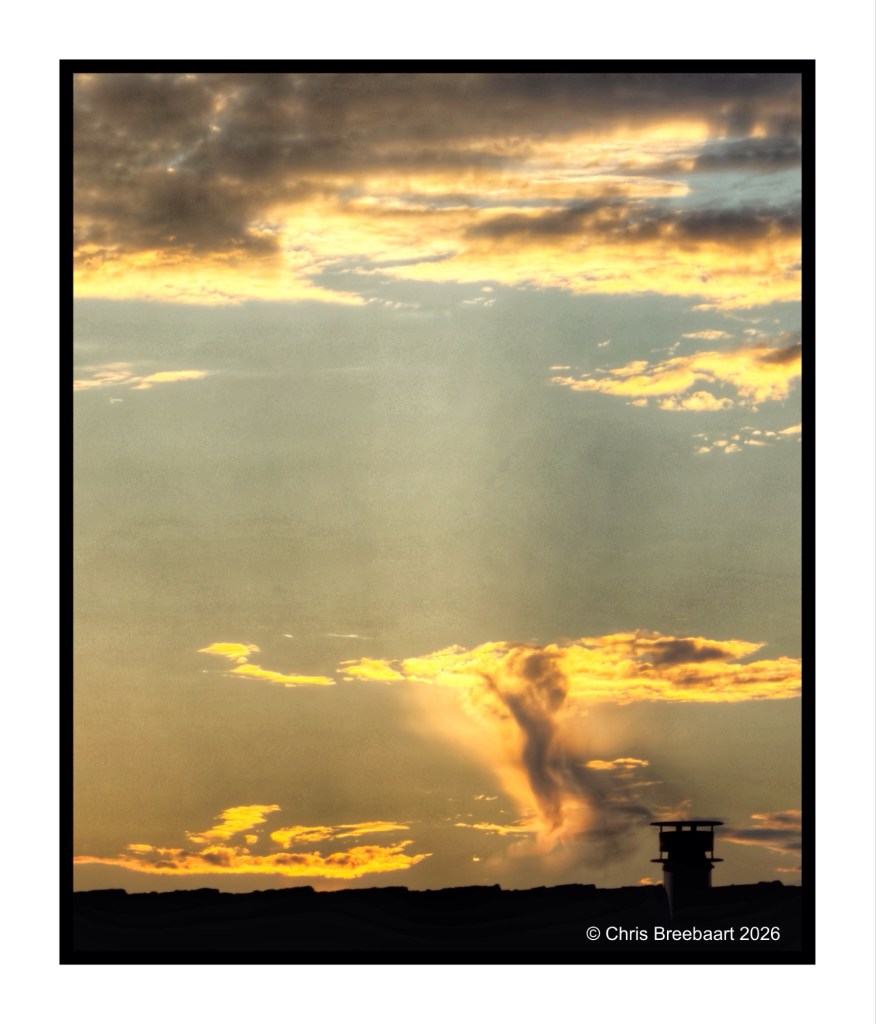 A dramatic sunset with vibrant orange and yellow hues illuminating clouds, alongside a silhouette of a tower in the foreground.