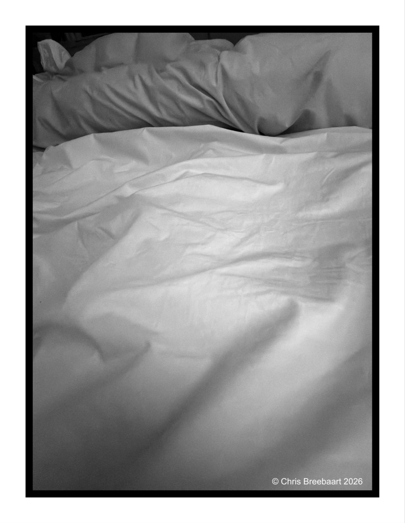 Wrinkled white sheets and pillows on a bed in black and white.