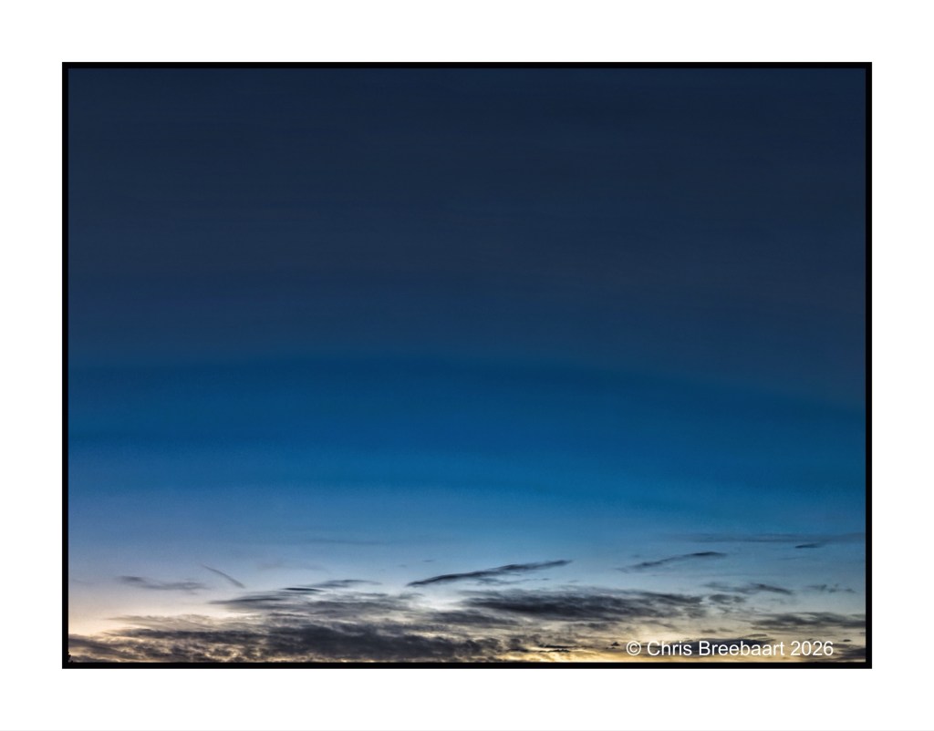 A serene twilight sky featuring deep blue and darker hues with soft, wispy clouds near the horizon.