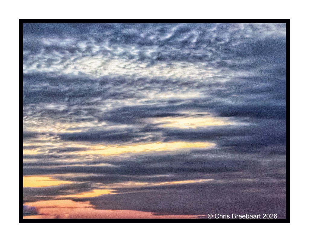 A dramatic sky filled with textured clouds in various shades of blue and gray, with hints of orange and yellow at the horizon during sunset.