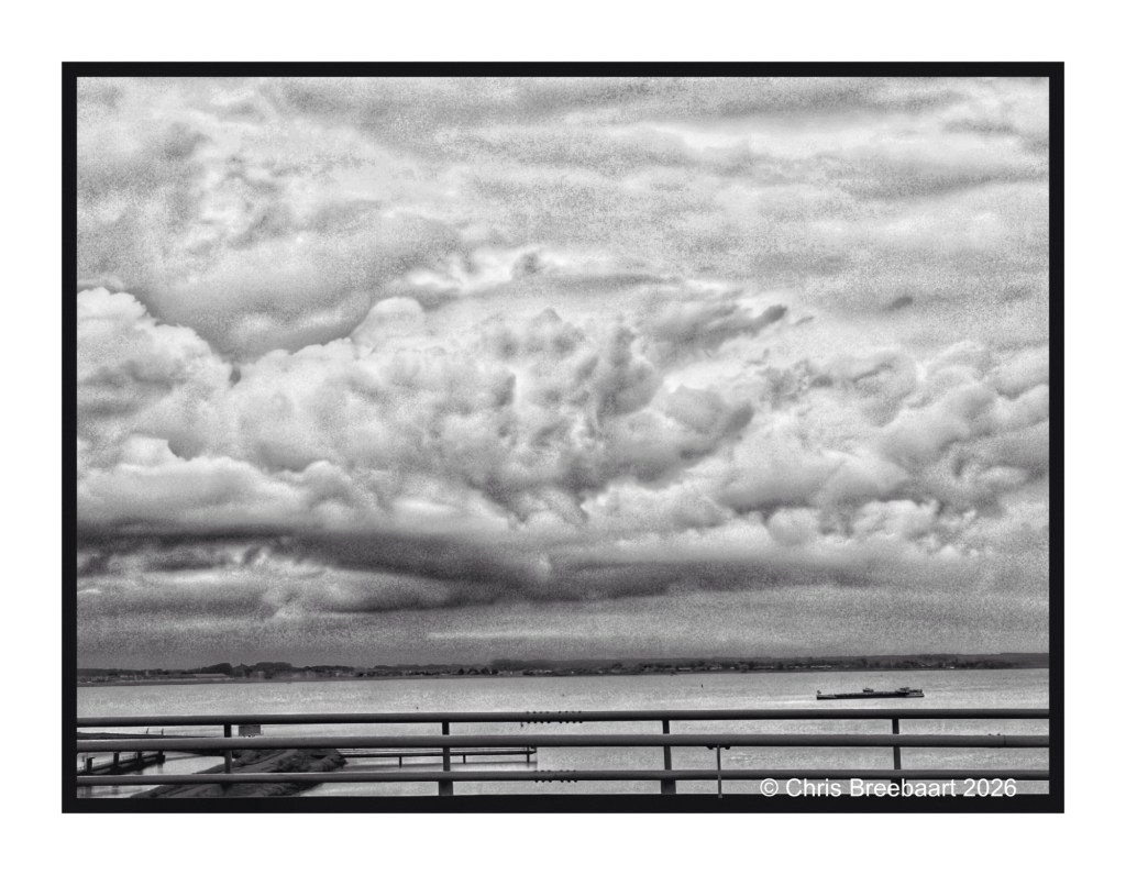 Black and white photograph of dramatic cloud formations over a calm body of water, with a small boat visible in the distance and a railing in the foreground.